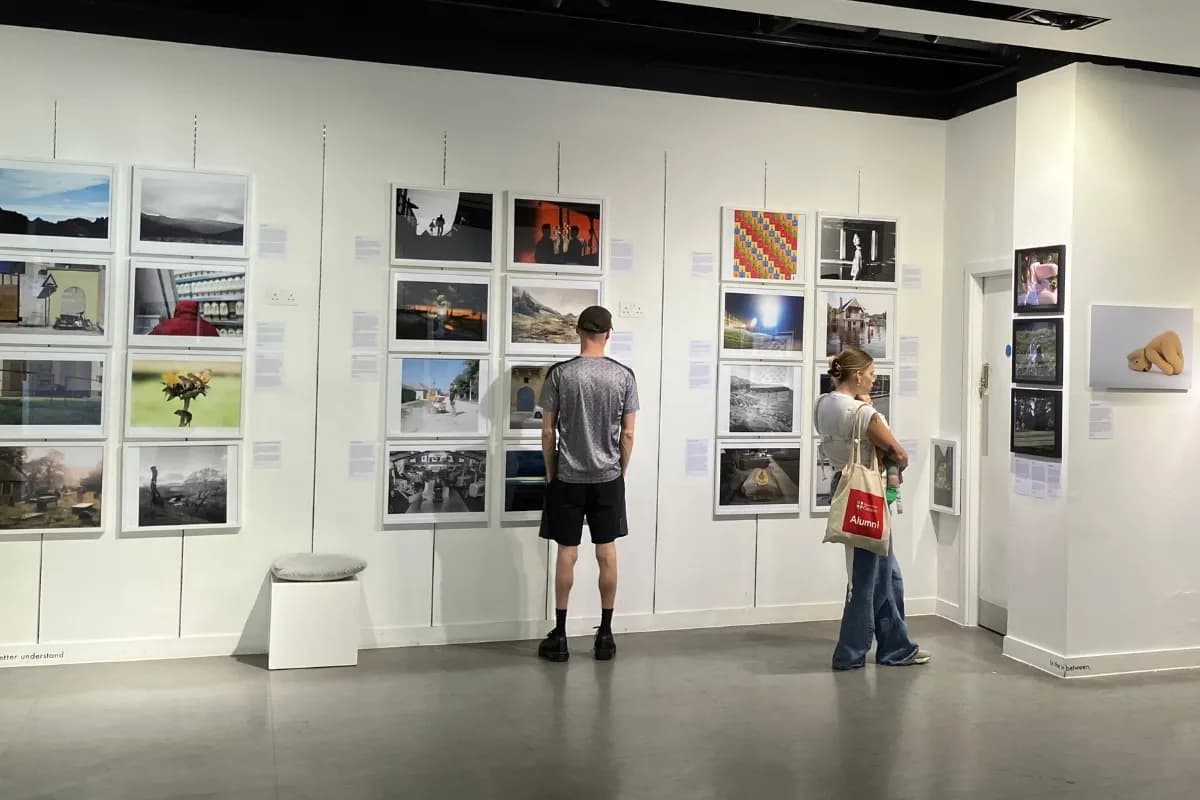 Two people are viewing an art exhibit with many framed photos displayed on a white wall in a bright room.